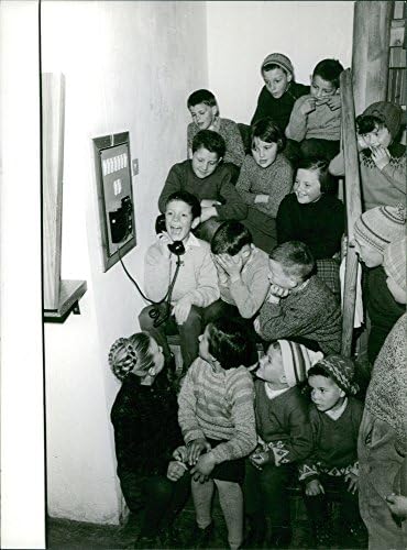 תצלום וינטג 'של ילד קטן מדבר בטלפון בזמן שאחרים מסתכלים ומחייכים אליו ב- Lavaredo.- 1963